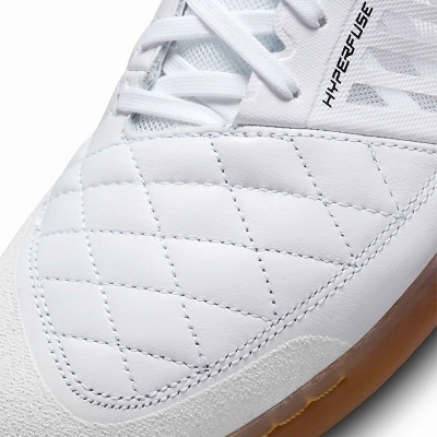 Detalhe de ténis desportivo branco com costura em losangos e sola castanha