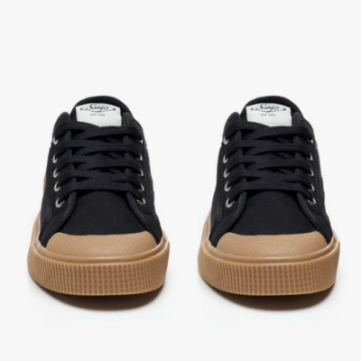 Ténis pretos com sola castanha e etiqueta branca com texto Kinja