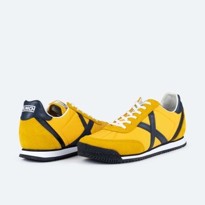 Sapatilhas amarelas com detalhes pretos e brancos, com sola preta e branca e nome MONICA na parte traseira