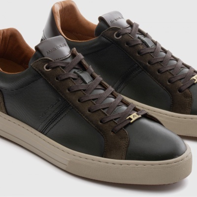 Sapatilhas de couro preto e camurça castanha com sola branca e detalhes dourados.