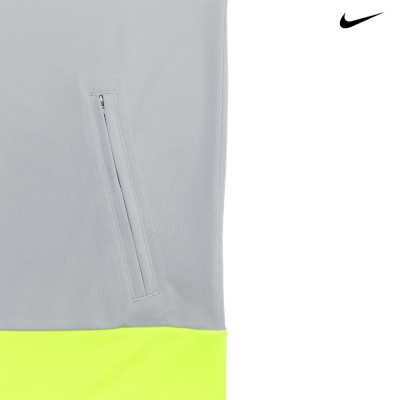Detalhe de peça de vestuário cinzenta com bolso e base amarela fluorescente e logotipo Nike.