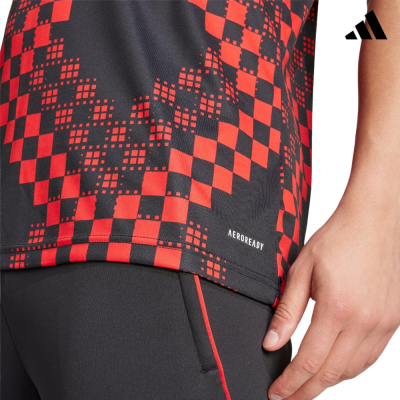 T-shirt desportiva preta e vermelha com padrão quadrado e texto AEROREADY, calças pretas com linha vermelha e mão ao lado.