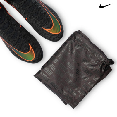 Chuteiras negras Nike com logo verde e laranja, ao lado de bolsa preta com padrão de texto Nike.
