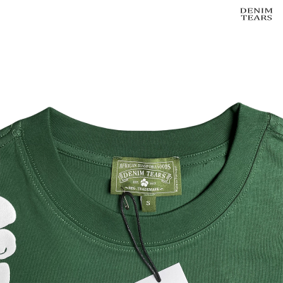 T-shirt verde com etiqueta da marca DENIM TEARS e texto de identificação.