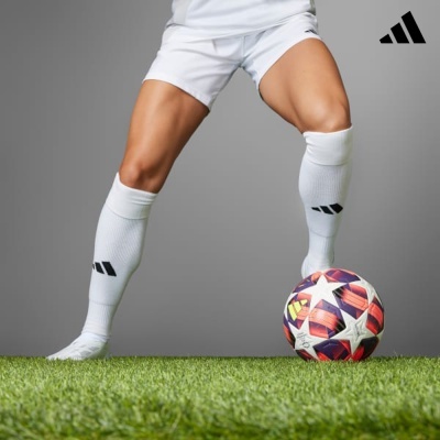 Jogador de futebol com calções e meias brancas a controlar bola colorida sobre relvado artificial