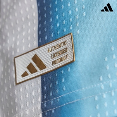 Etiqueta metálica dourada em tecido azul claro e branco com padrão e logo Adidas preto