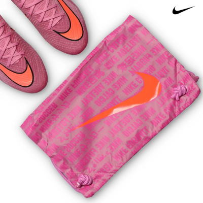 Bolsa desportiva rosa com texto NIKE e logotipo Swoosh laranja ao lado de sapatos de futebol cor-de-rosa.