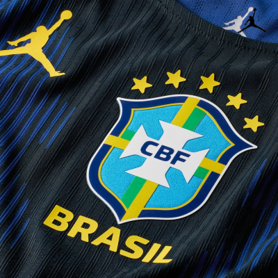 Emblema da seleção brasileira CBF em camisola preta e azul com cinco estrelas amarelas e texto Brasil.