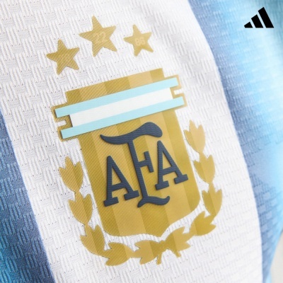 Emblema da AFA em camisola branca e azul da Adidas com três estrelas douradas.