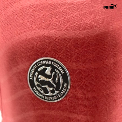 Tecido vermelho com padrão geométrico e medalha metálica com texto Authentic Licensed Football e logotipo Puma