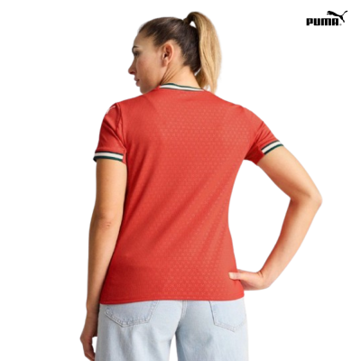 T-shirt vermelha com riscas verde e branco na gola e punhos, vista de costas, usada com calças de ganga claras.