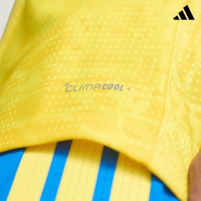 Tecido amarelo com textura e texto CLIMACOOL +, riscas azuis e amarelas e logótipo Adidas