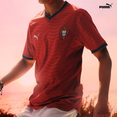 Camisola de futebol vermelha PUMA da seleção de Portugal com brasão e gola em V verde.