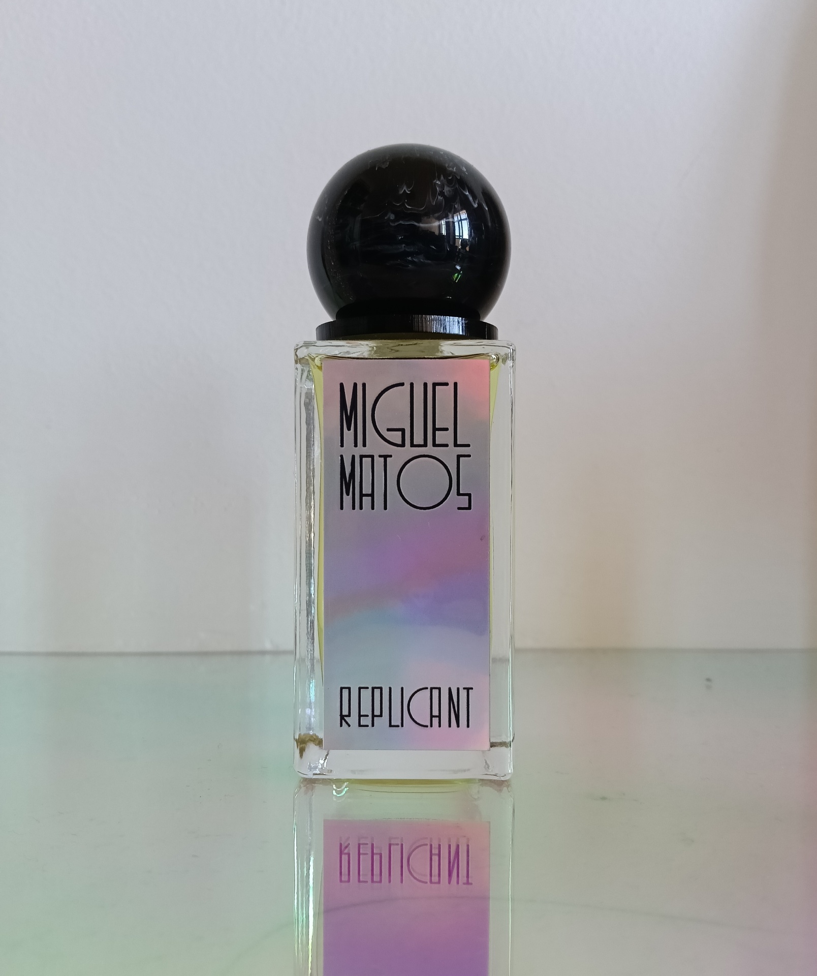 Rectangular glass perfume bottle with black spherical cap and holographic label