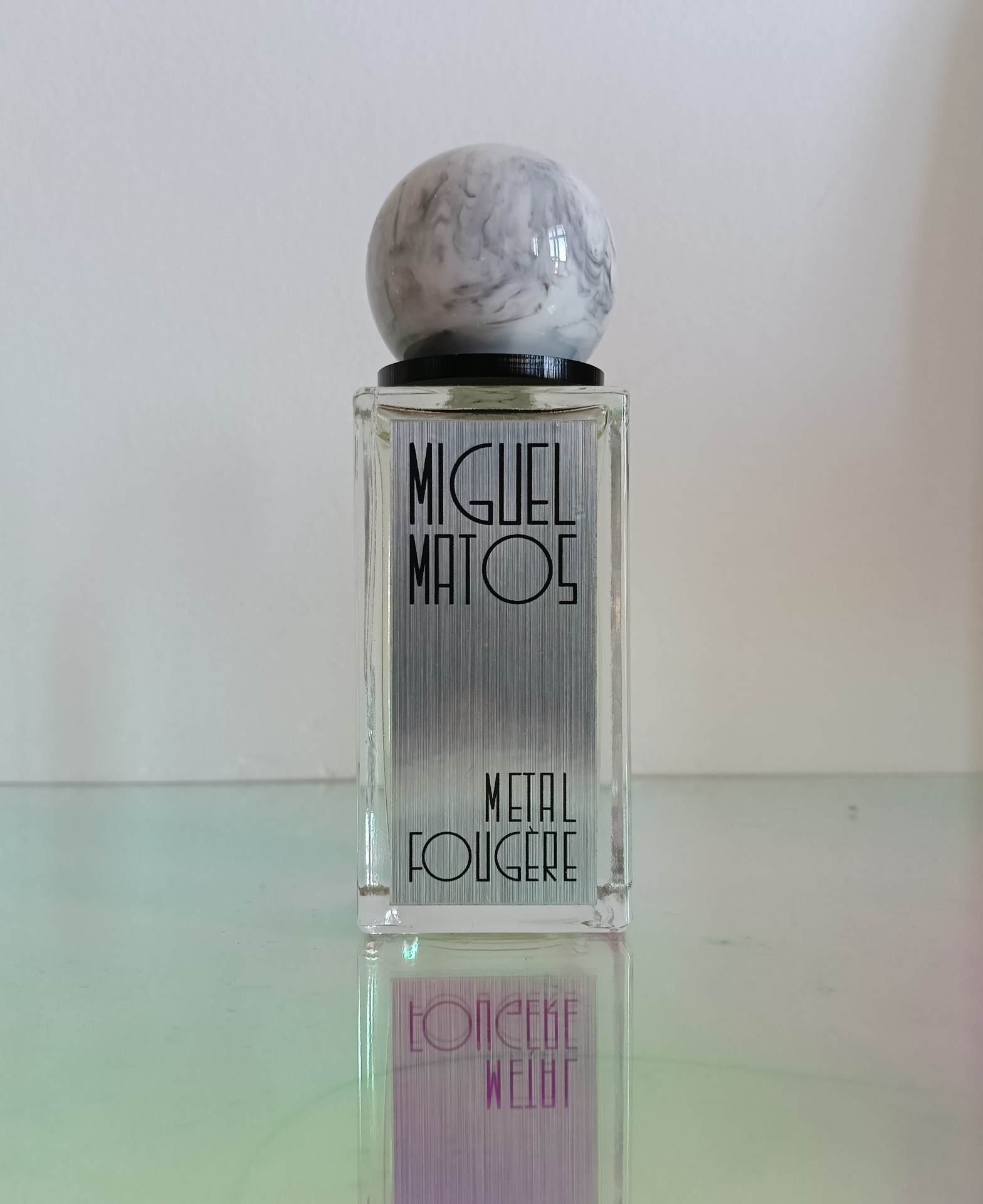 Clear glass perfume bottle with metallic label and marbled round cap