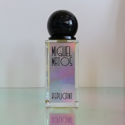 Rectangular glass perfume bottle with black spherical cap and holographic label