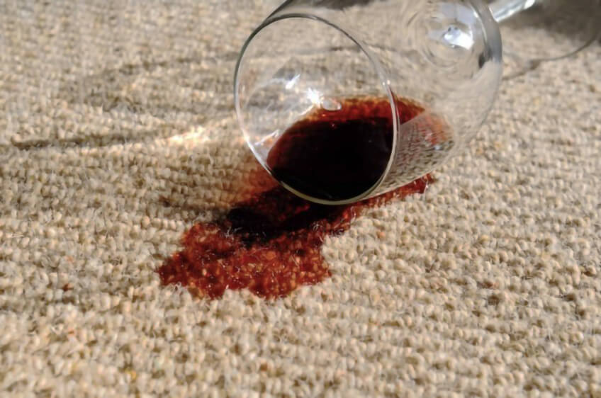 Copo de vidro tombado com vinho tinto derramado em tapete bege