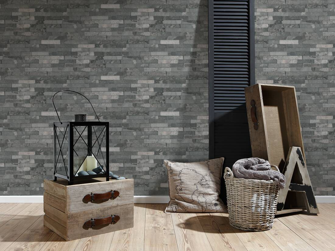 Papel de Parede Pedra, Casa de Campo, Bege, Preto, Cinzento 35582-4 Conjunto decorativo com caixa de madeira, lanterna preta, almofada, cesta com manta, caixa e letra A junto a uma parede de tijoleira cinza