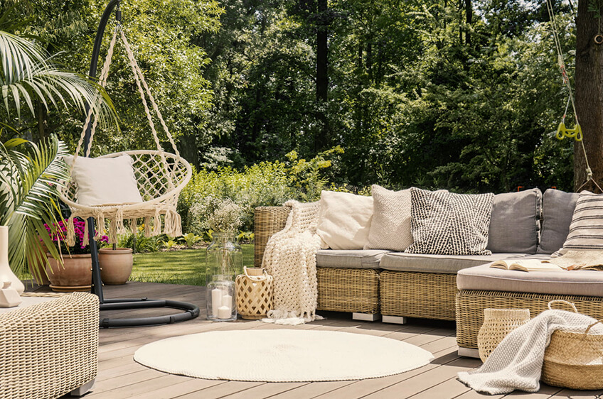 Móveis de exterior em rattan com almofadas, cadeira suspensa de vime e plantas num deck de madeira