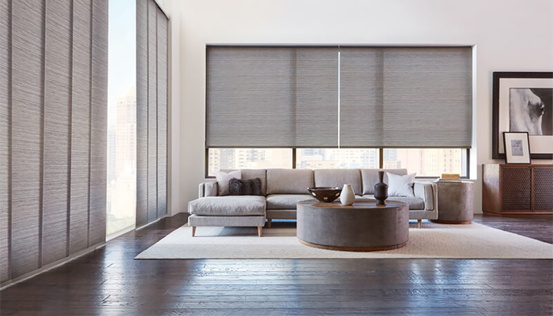 Sala de estar com sofá cinza, persianas cinza, mesa de centro redonda e quadro a preto e branco