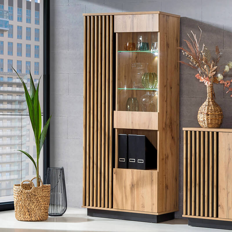 Vitrine com três Portas Carvalho e Preto Lamelo Armário alto de madeira clara com prateleiras e portas, decorado com plantas ao lado de janela grande