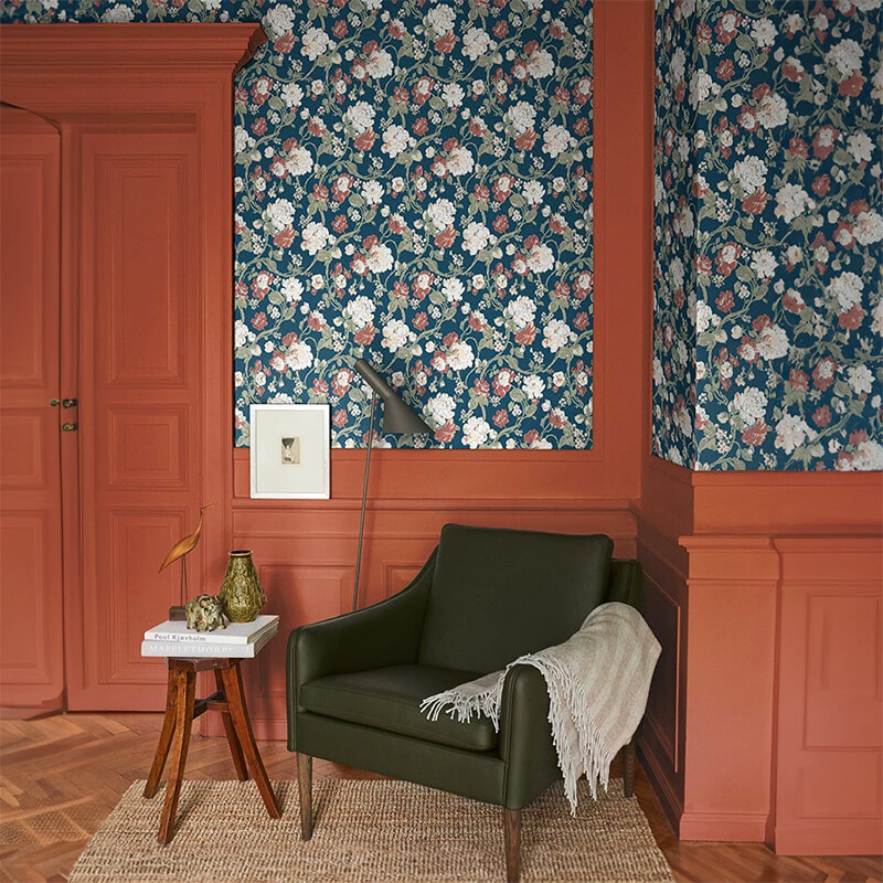 Papel de Parede Impressionism Fiona Wall Design | 600210 Poltrona verde escuro com manta sobre tapete bege, parede florida azul e porta cor terra.