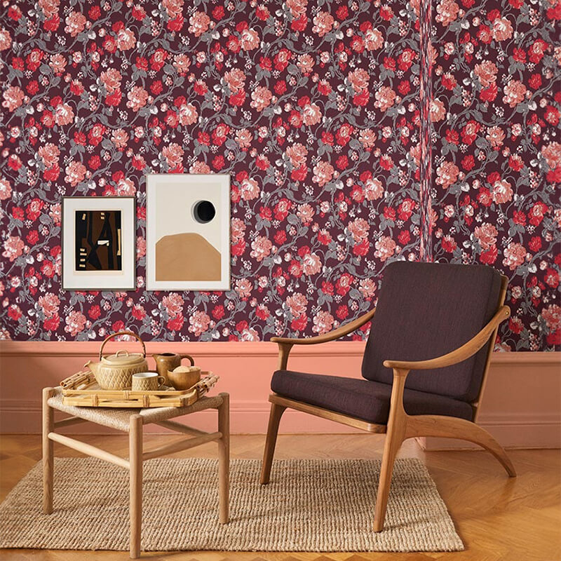 Papel de Parede Impressionism Fiona Wall Design | 600209 Poltrona em madeira clara com almofada roxa e mesinha de apoio transparente com utensílios de madeira, tapete bege, parede com papel de parede floral vinho e quadros.