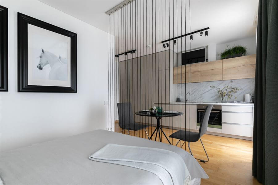 Estúdio moderno com cama, divisória de fios, mesa e cadeiras, cozinha integrada e quadro de cavalo