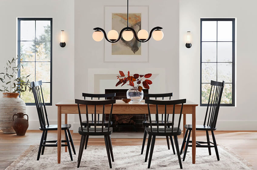 Sala de jantar com mesa de madeira, seis cadeiras pretas, vaso com folhas vermelhas e candeeiro moderno