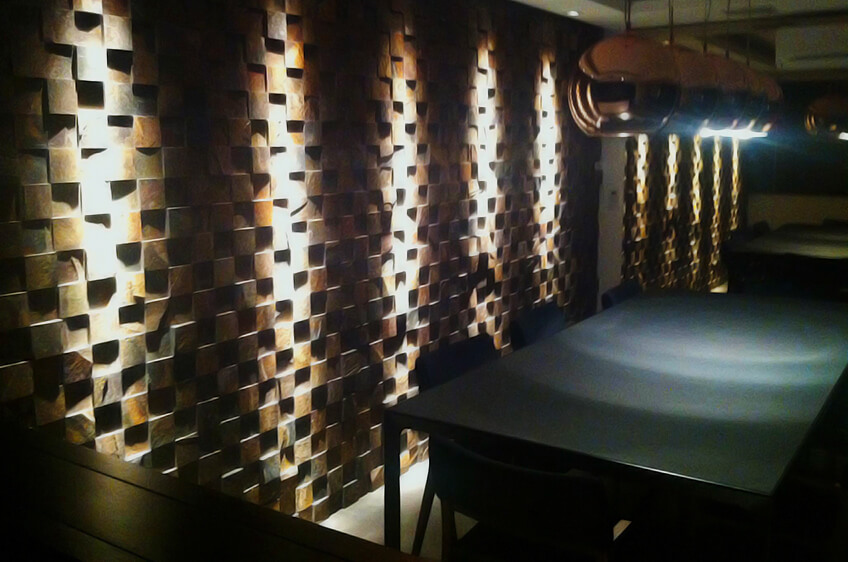 Mesa preta com cadeiras junto a parede de blocos tridimensionais castanhos