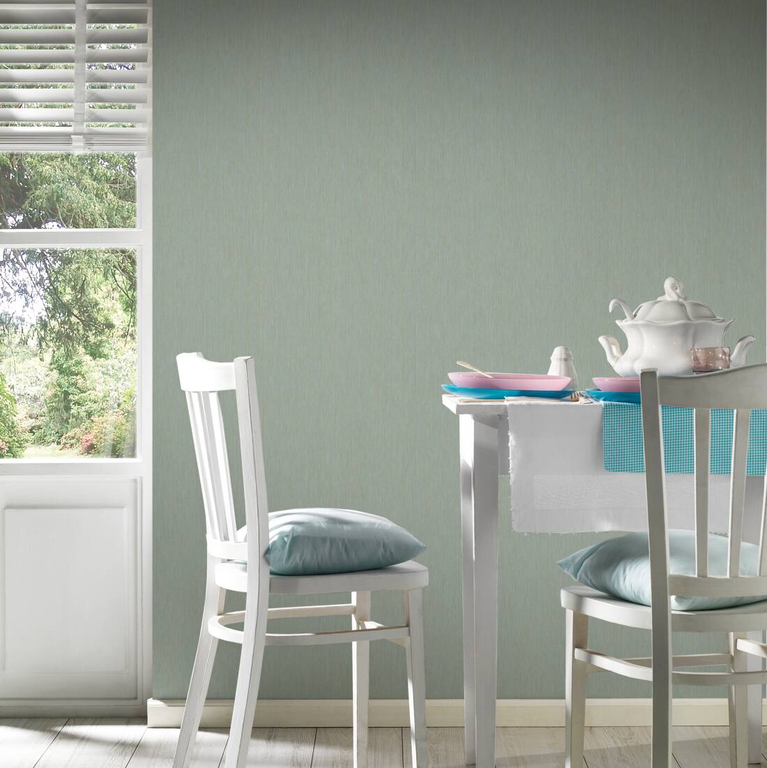 Papel de Parede Tropical, Folhas, Uni, Dourado, Verde, Metálico 37375-6 Mesa de jantar com loiça branca e azul, cadeiras brancas e almofadas azuis junto a porta e parede verde