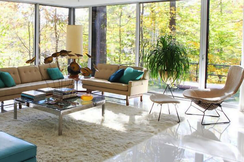 Sala de estar moderna com sofá bege, mesa de centro de vidro e grandes janelas