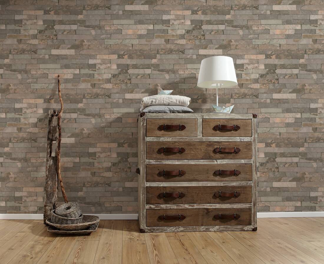 Papel de Parede Pedra, Casa de Campo, Bege, Castanho 35582-2 Móvel de madeira envelhecida com seis gavetas contra parede de tijolos cinzentos e marrons e chão de madeira clara