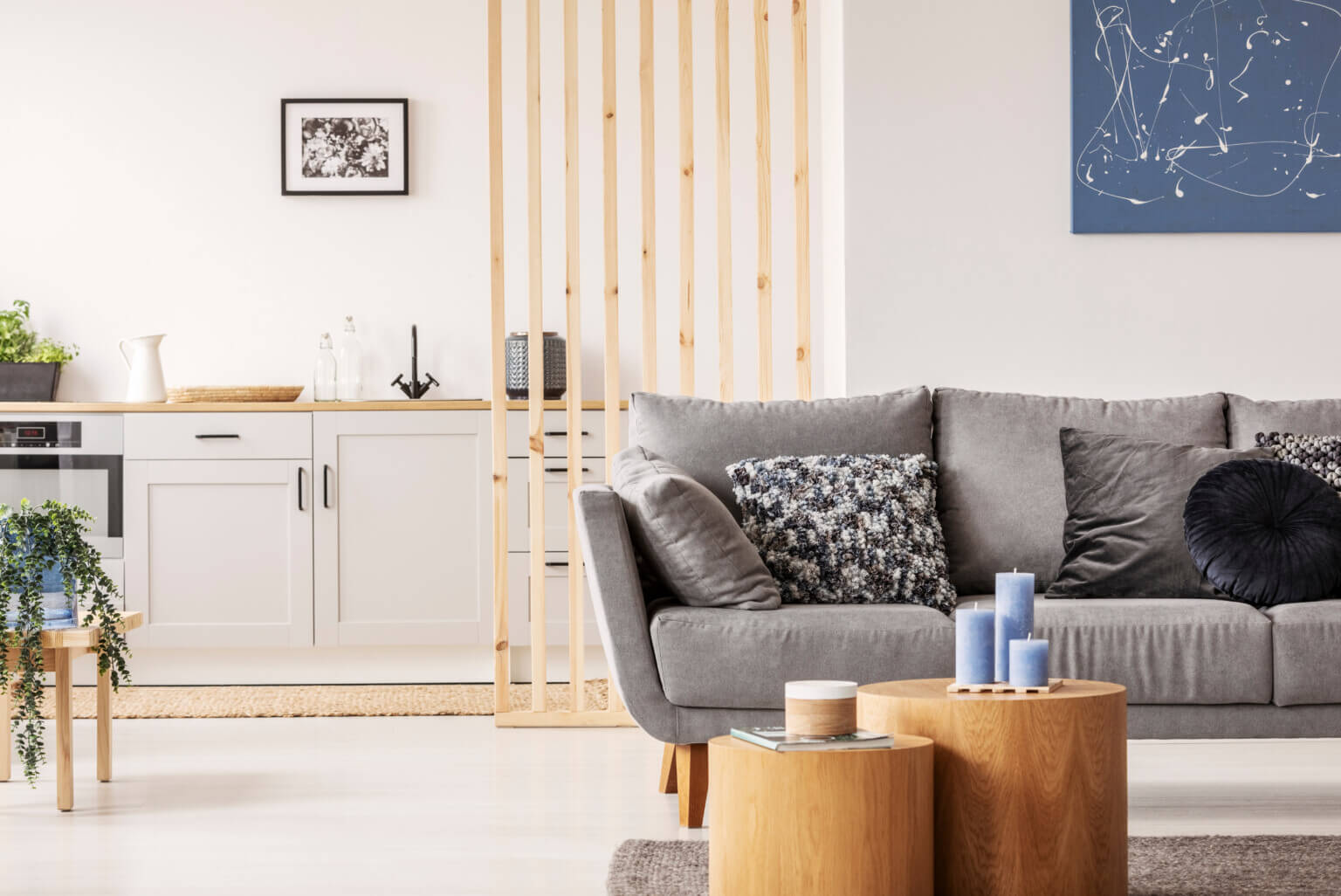 Sala de estar com sofá cinzento, almofadas, mesas de madeira e cozinha ao fundo