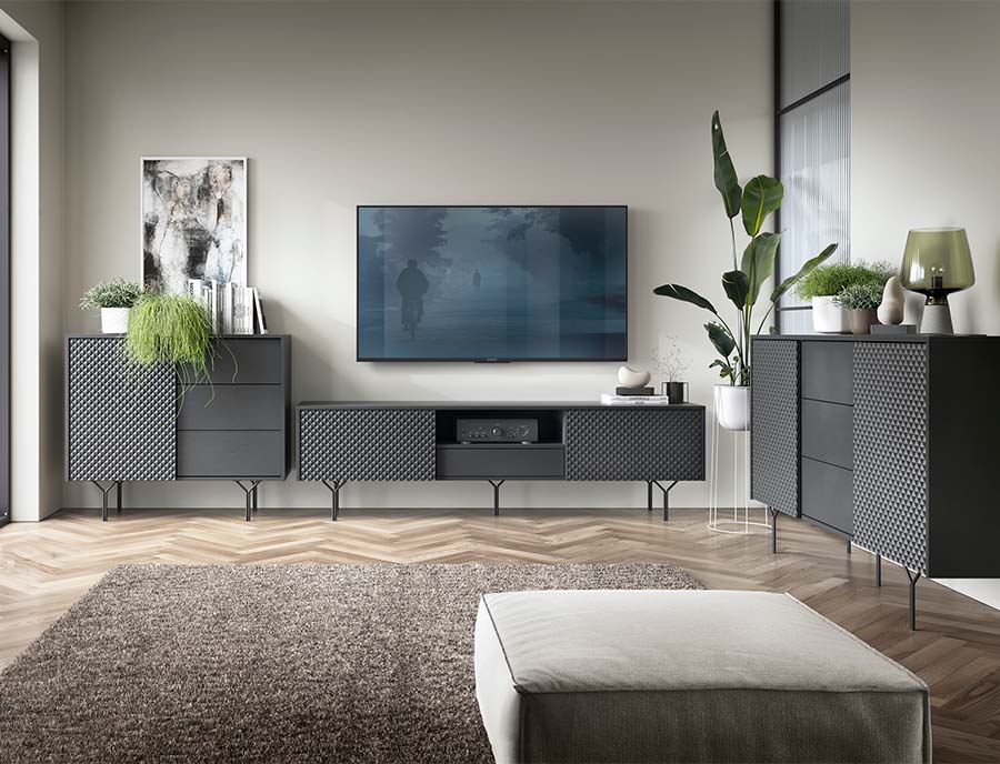 Sala de estar com móveis pretos texturizados, tapete castanho, televisão na parede e plantas