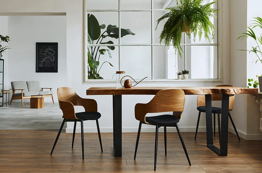 Mesa de jantar rústica com cadeiras de madeira e almofadas pretas em interior com plantas