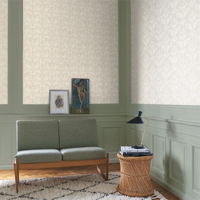 Sala com sofá verde, mesa em rattan com candeeiro e duas molduras apoiadas no sofá