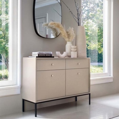 Aparador bege com gavetas e objetos decorativos em ambiente interior com janelas grandes