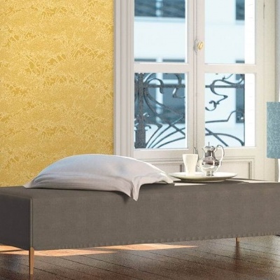 Banco estofado cinza com almofada e bandeja, parede amarela com padrão floral, janela branca com ferro preto.