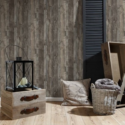 Decoração interior com caixas de madeira, lanterna preta, almofada bege, cesta de vime e manta cinza junto a uma parede de madeira cinzenta