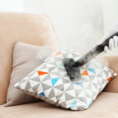 Almofada com padrão geométrico sendo limpa a vapor num sofá bege