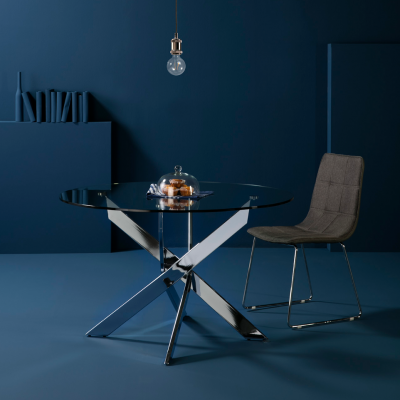 Mesa redonda de vidro com pés metálicos e cadeira cinza em ambiente azul escuro com luminária pendente
