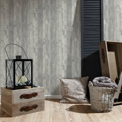 Arranjo decorativo com gavetas de madeira, lanterna preta, almofada com mapa, cesta de vime com manta e parede com papel de parede cinza padrão madeira.