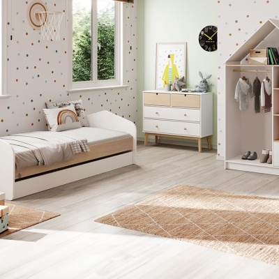 Quarto infantil com cama, cómoda e estante branca e madeira clara, paredes com pontos coloridos, tapetes castanhos e janela para jardim