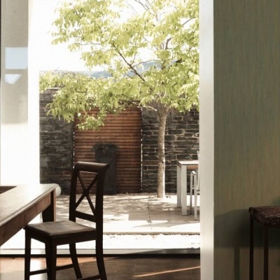 Interior com mesa de madeira, cadeira, e vista para pátio com cerca de pedra e árvore