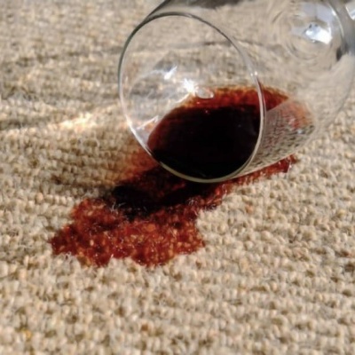 Copo de vidro tombado com vinho tinto derramado em tapete bege