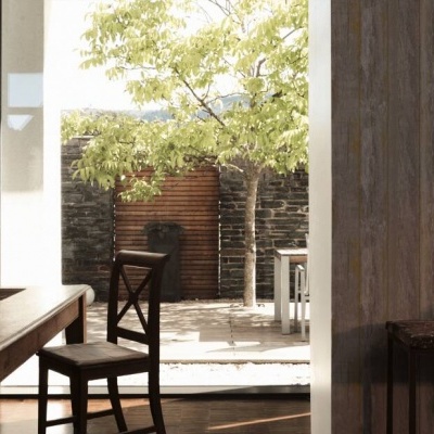Mesa de madeira com cadeira num interior rústico com vista para exterior com árvore e barril