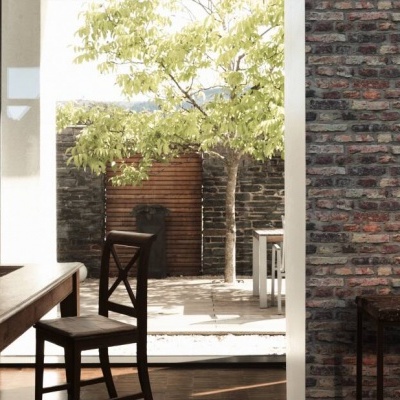 Sala com mesa e cadeira de madeira junto a parede de tijolo com porta aberta para pátio com árvore e vaso