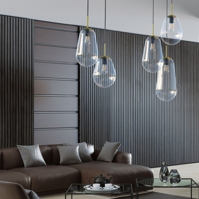 Candeeiros suspensos de vidro transparente com detalhes dourados num interior moderno com sofá castanho e paredes cinzentas texturizadas