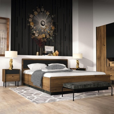 Quarto moderno com cama de madeira, mesas de cabeceira, candeeiros dourados, banco em veludo verde e decoração metálica na parede.